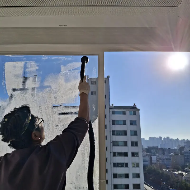 작업자가 고층 주거 공간의 창 유리 전면에 세제를 도포하는 모습
