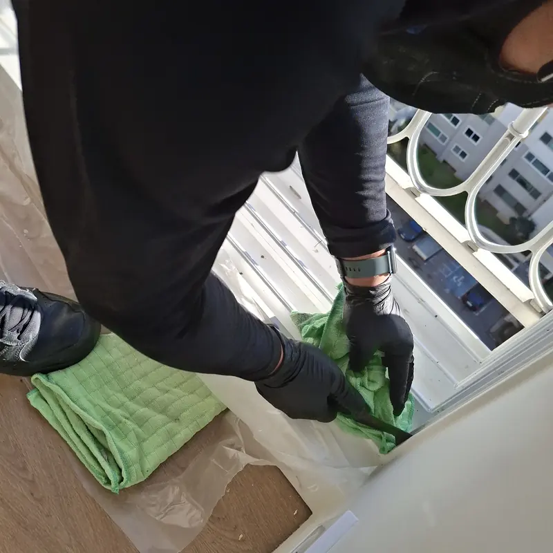 무릎을 꿇은 작업자가 주거 공간 창틀 레일을 초록색 걸레로 닦는 모습