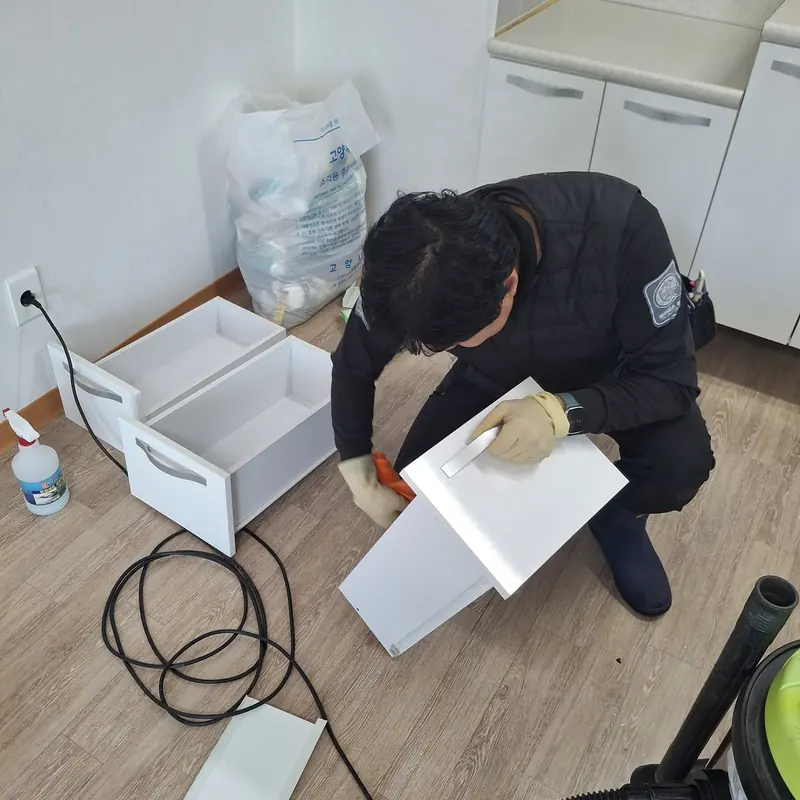 작업자가 바닥에 빼놓은 흰색 서랍의 안팎을 걸레로 닦는 모습