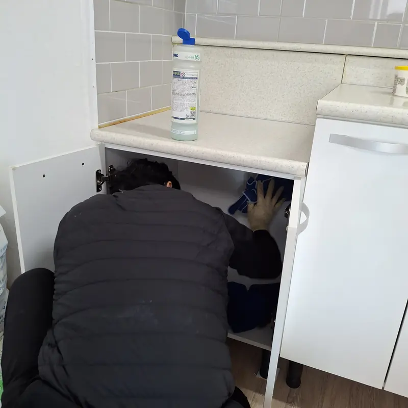 작업자가 몸을 숙여 싱크대 하부장 안쪽 바닥과 벽면을 닦는 모습