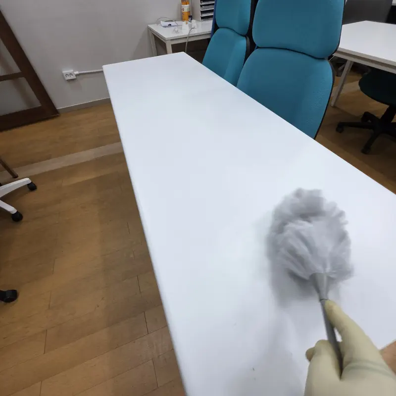 장갑을 낀 손이 먼지털이개로 책상 상판의 가루를 바닥 쪽으로 쓸어내는 모습