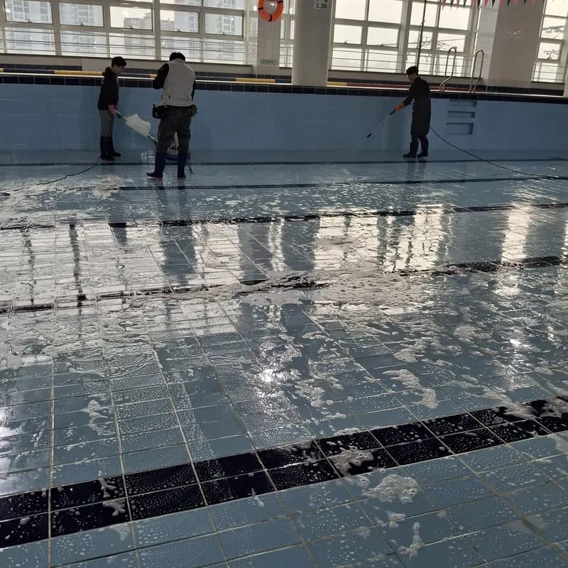 물을 뺀 실내 수영장 바닥 타일을 두 작업자가 세제를 풀어 세척하는 현장