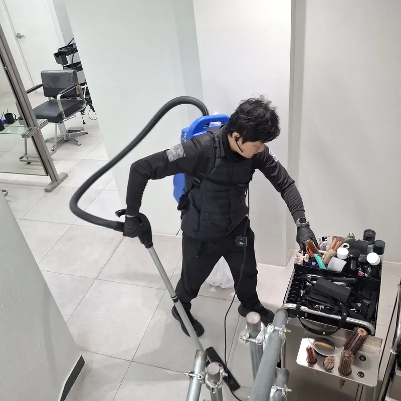 미용실 시술석 사이 바닥을 업소용 진공청소기로 흡입하는 작업자