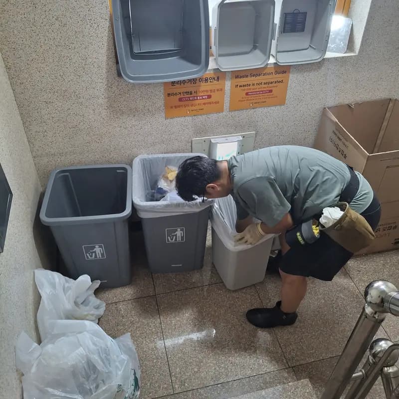 작업자가 건물 분리배출 구역에서 쓰레기통 봉투를 종류별로 정리하는 모습