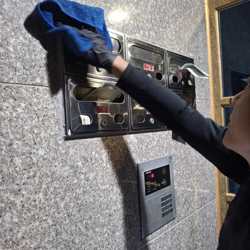 장갑을 낀 손이 공동현관 벽면의 인터폰과 우편함 표면을 걸레로 닦는 모습